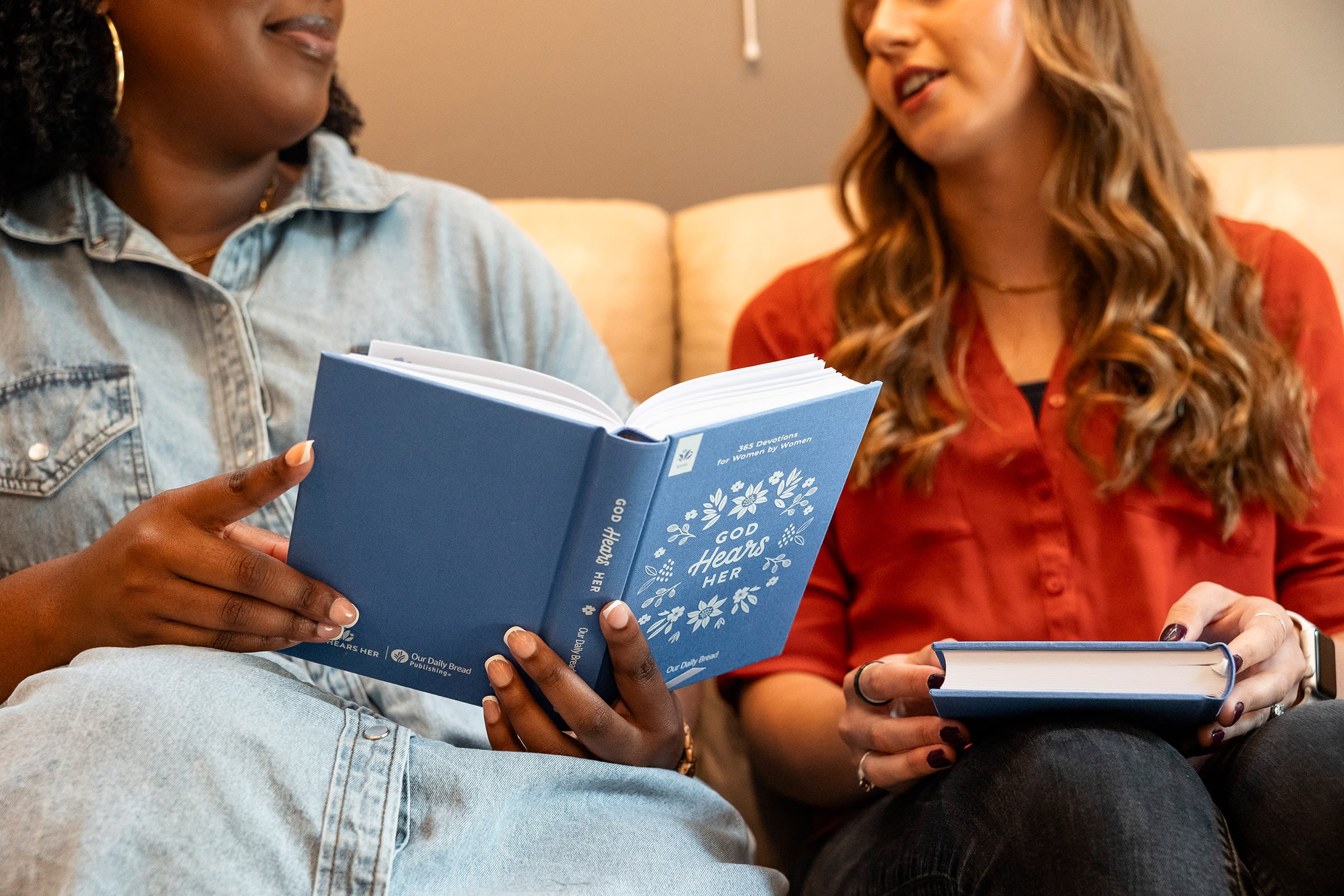 Two women reading books on a couch.